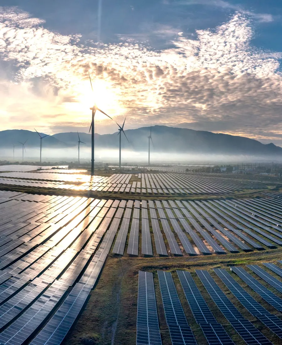 Aerial view of a solar farm with wind turbines at sunrise